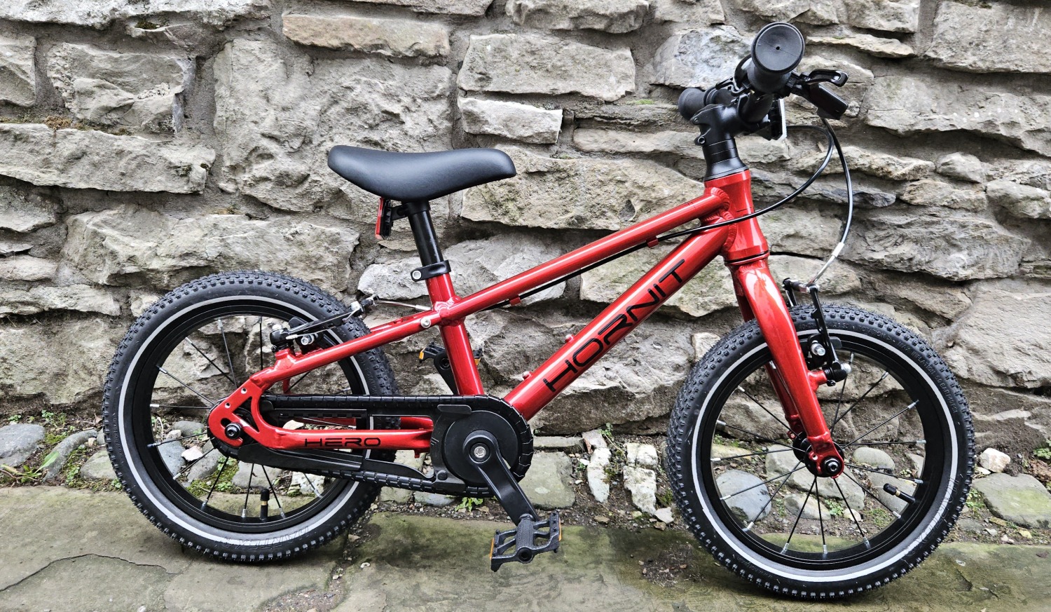Hornit HERO 14 kids pedal bike side view of the bike resting against a stone wall