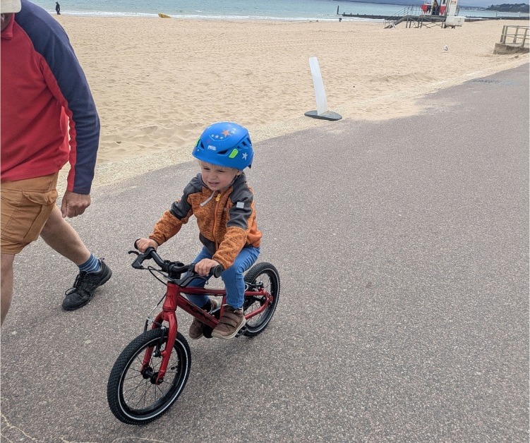 Hornit HERO 14 red kids bike being ridden by a young boy on a paved path next to the beach 