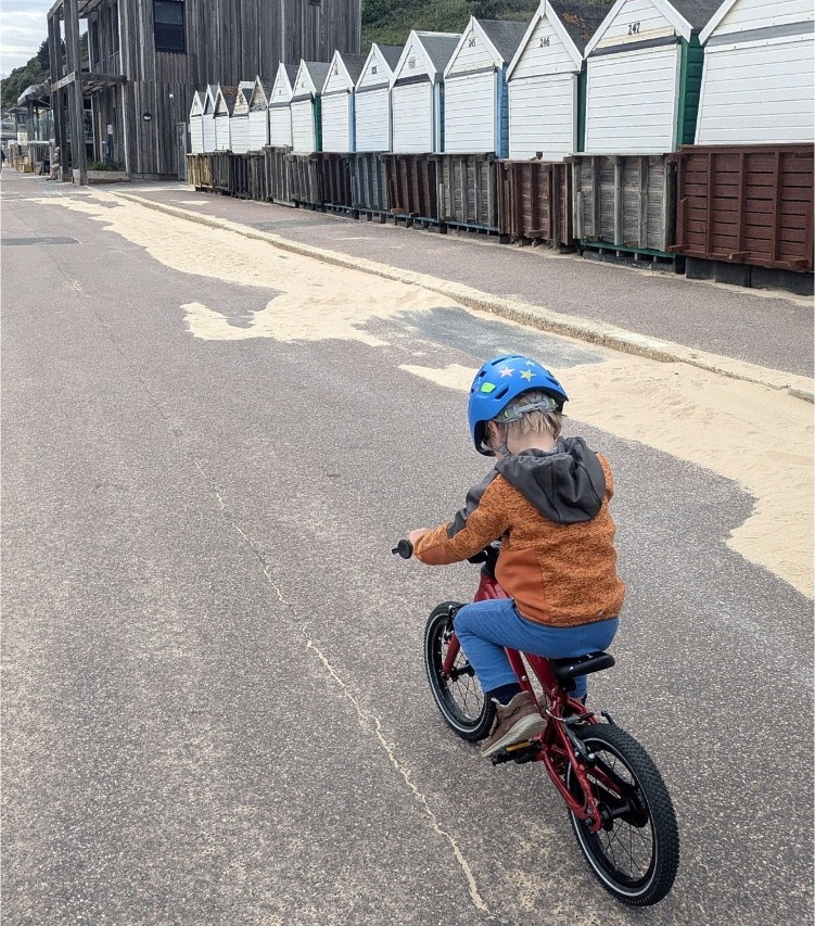 Red Hornit HERO 14 kids bike being ridden by the beach along a paved path past some beach huts