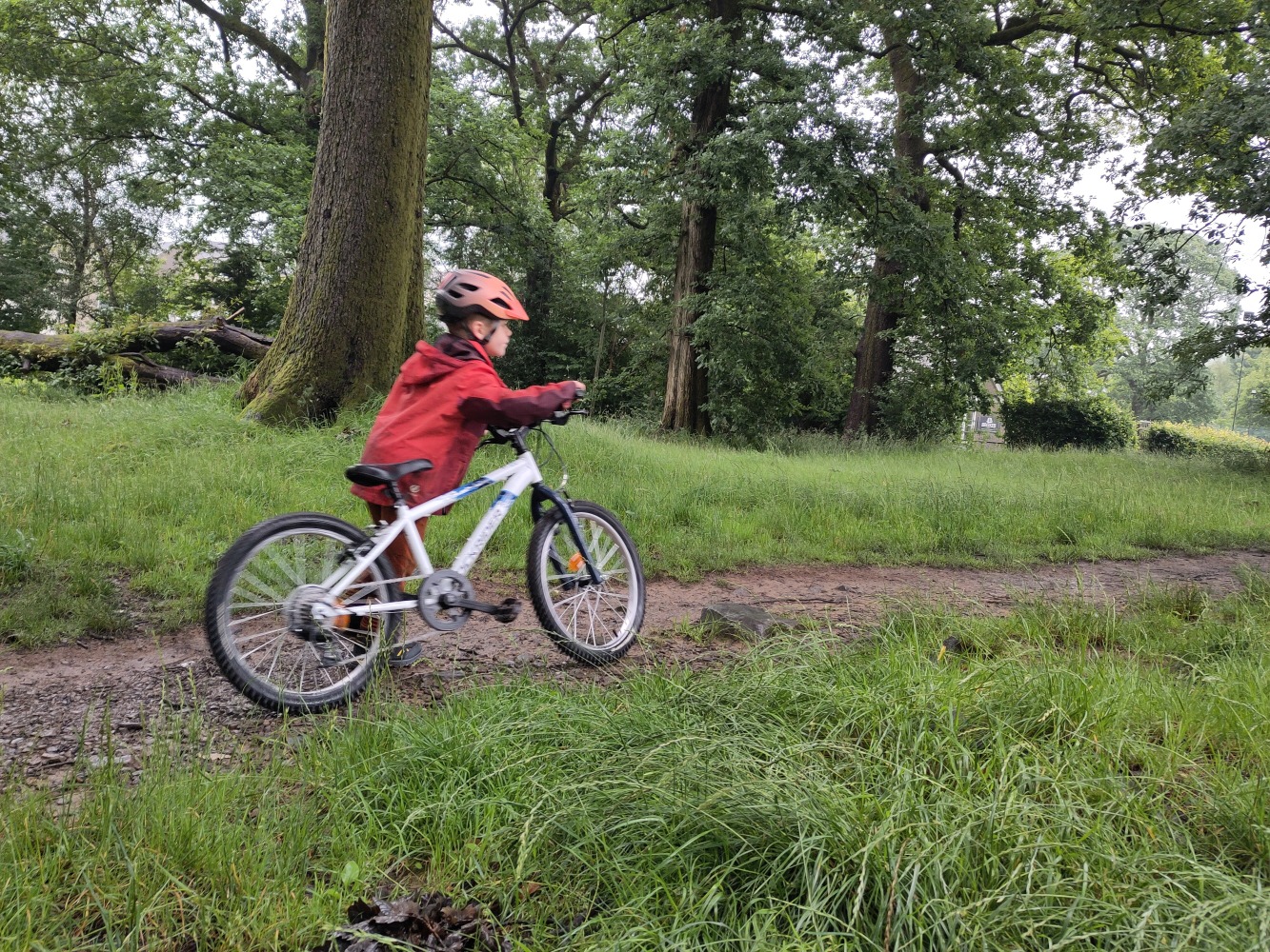 Young boy in a red coat pushing the Rockrider 20" MTB Expl 120 along a dirt path in a wooded area