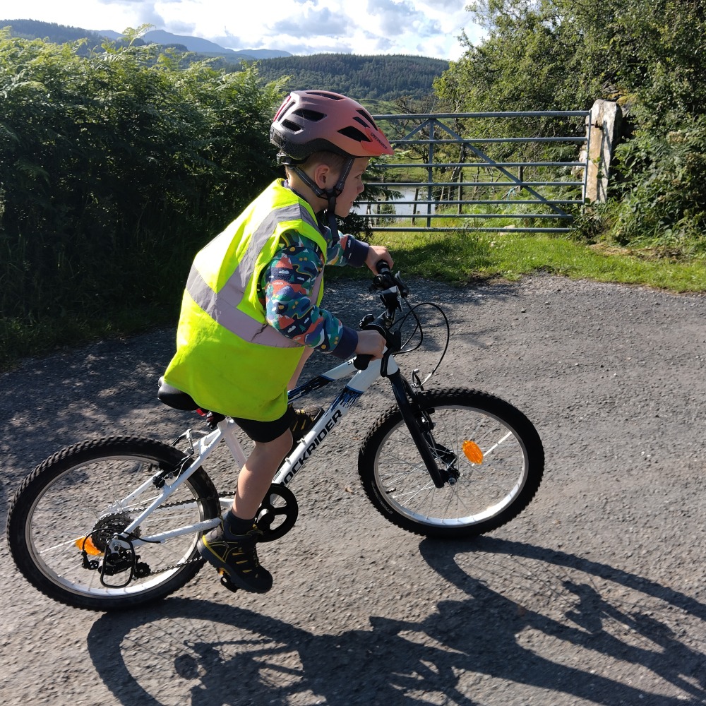 Young boy in a hi-vis vest riding the Rockrider 20" MTB Expl 120 kids bike on a paved road