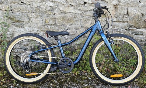 Side on view of the Ridgeback Dimension 20 kids bike leant against a stone wall