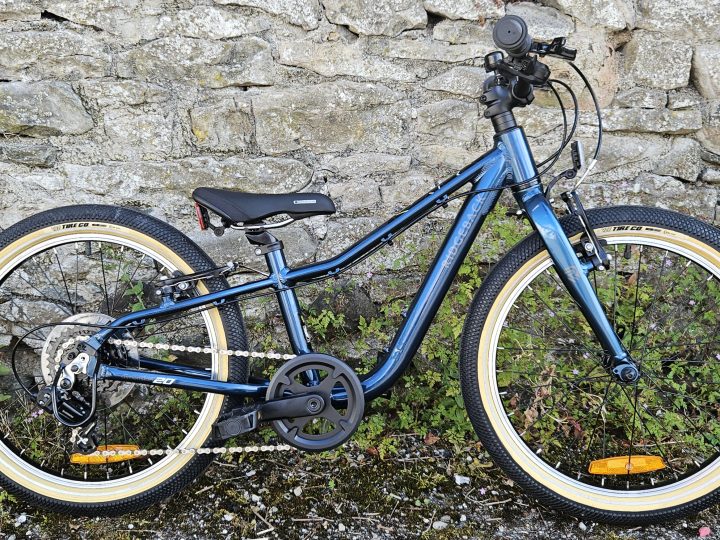 Side on view of the Ridgeback Dimension 20 kids bike leant against a stone wall
