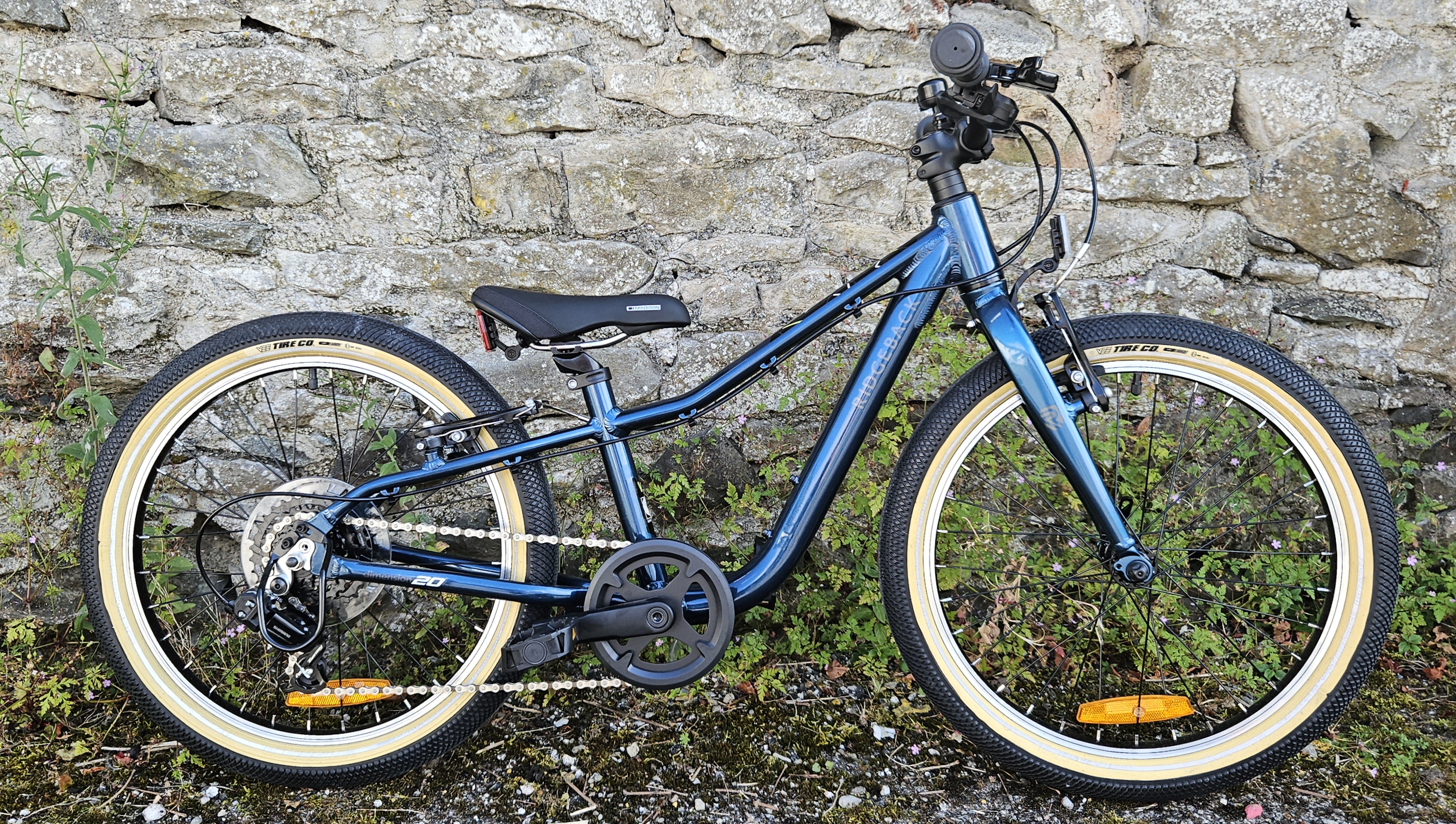 Side on view of the Ridgeback Dimension 20 kids bike leant against a stone wall