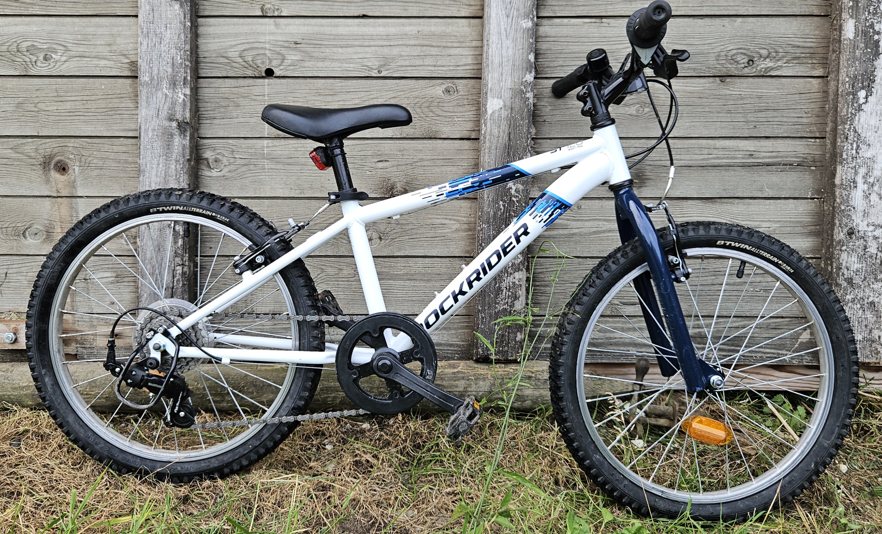 Rockrider 120 kids bike leant against a fence with full side on view of the bike