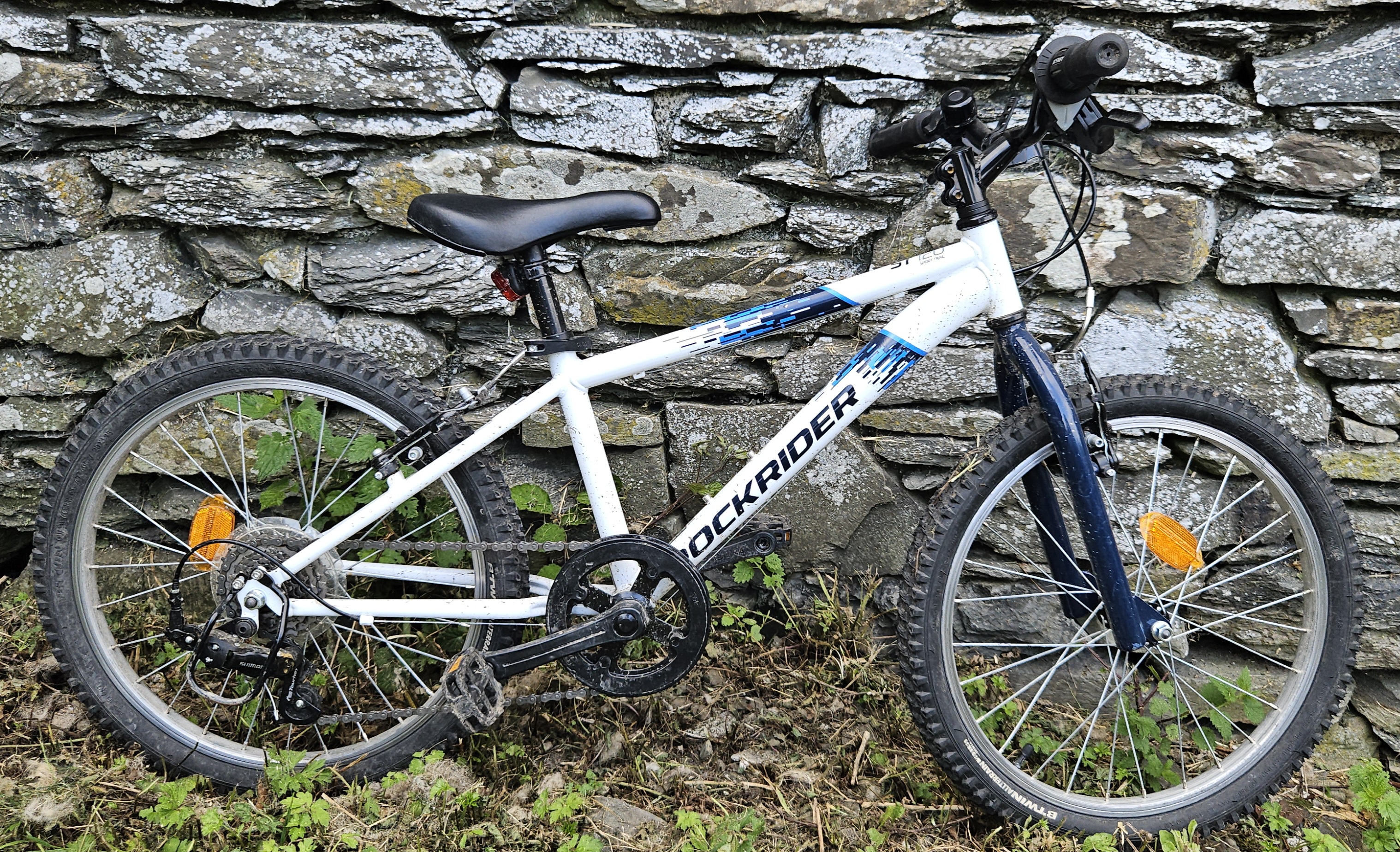 Side on view of the Rockrider 120 kids bike leant against a stone wall