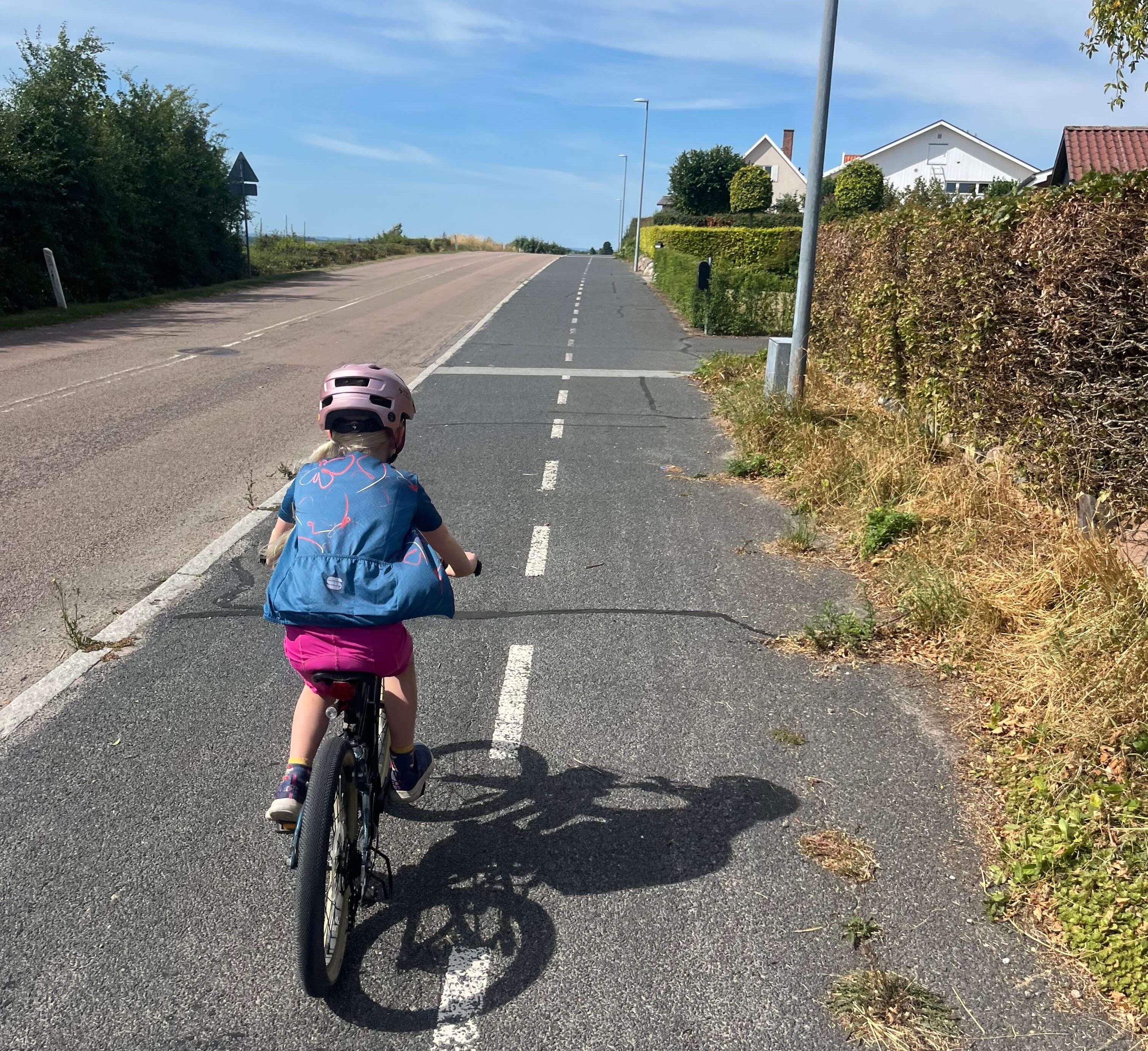 Ridgeback Dimension 20 kids bike being ridden up a hill by a young girl dressed in pink wearing a backpack