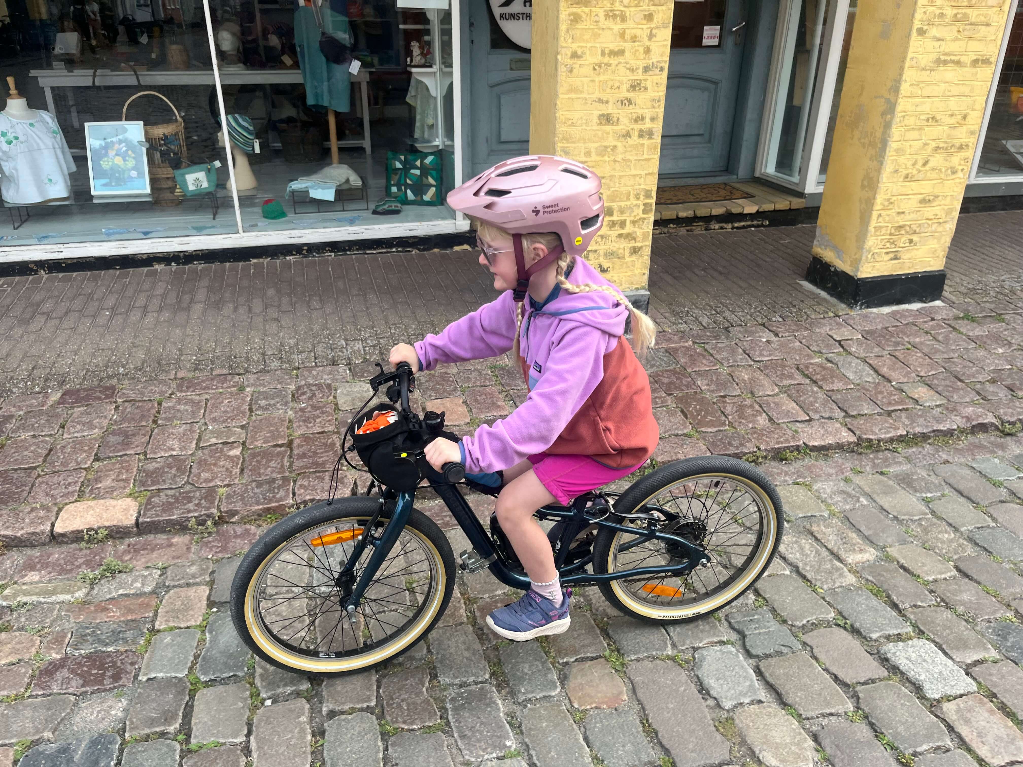 Ridgeback Dimension 20 kids bike being ridden by a young girl in a pink outfit along a cobbled street