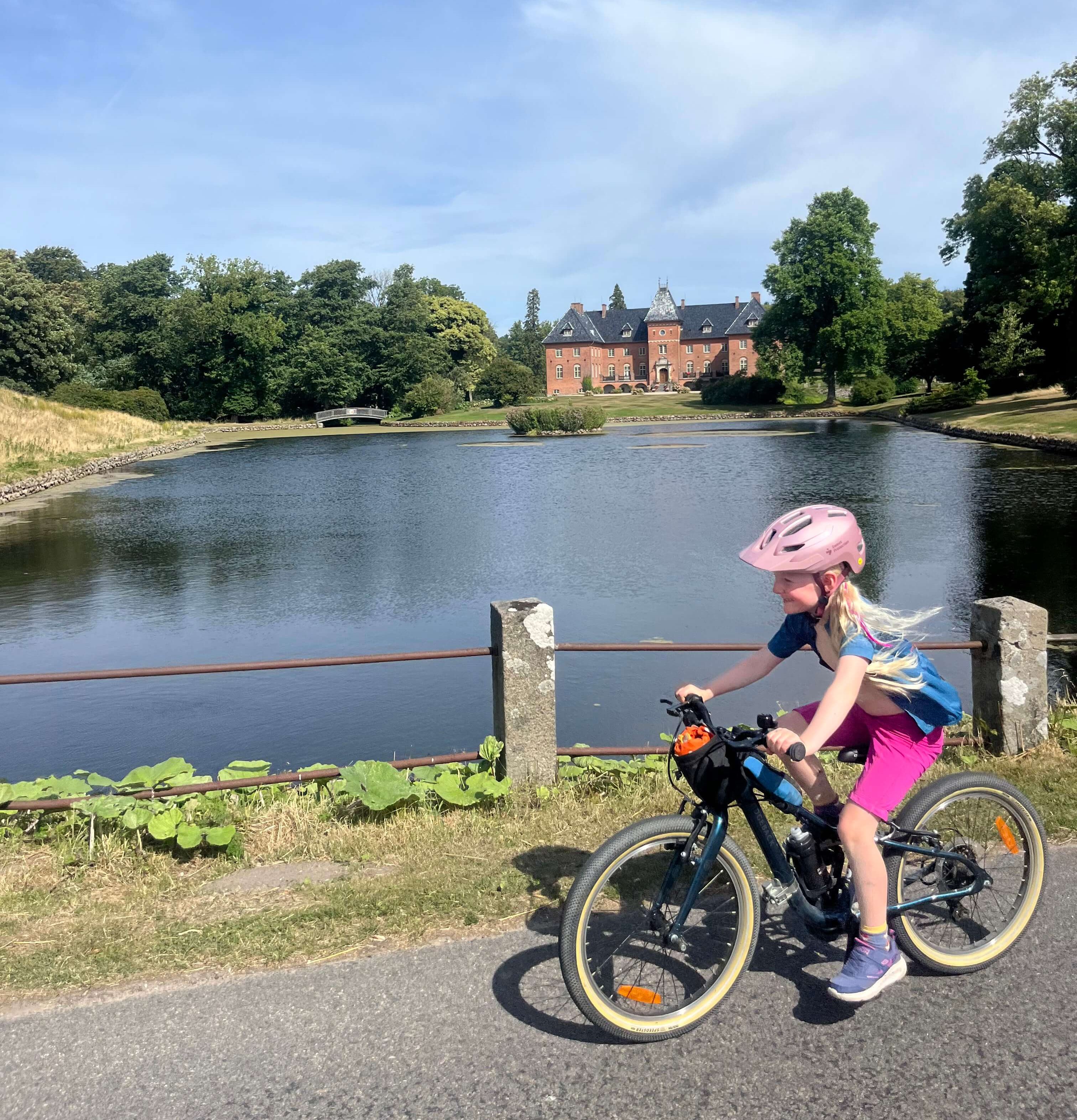 Ridgeback Dimension 20 kids bike being ridden by a young girl wearing a pink helmet beside a lake 