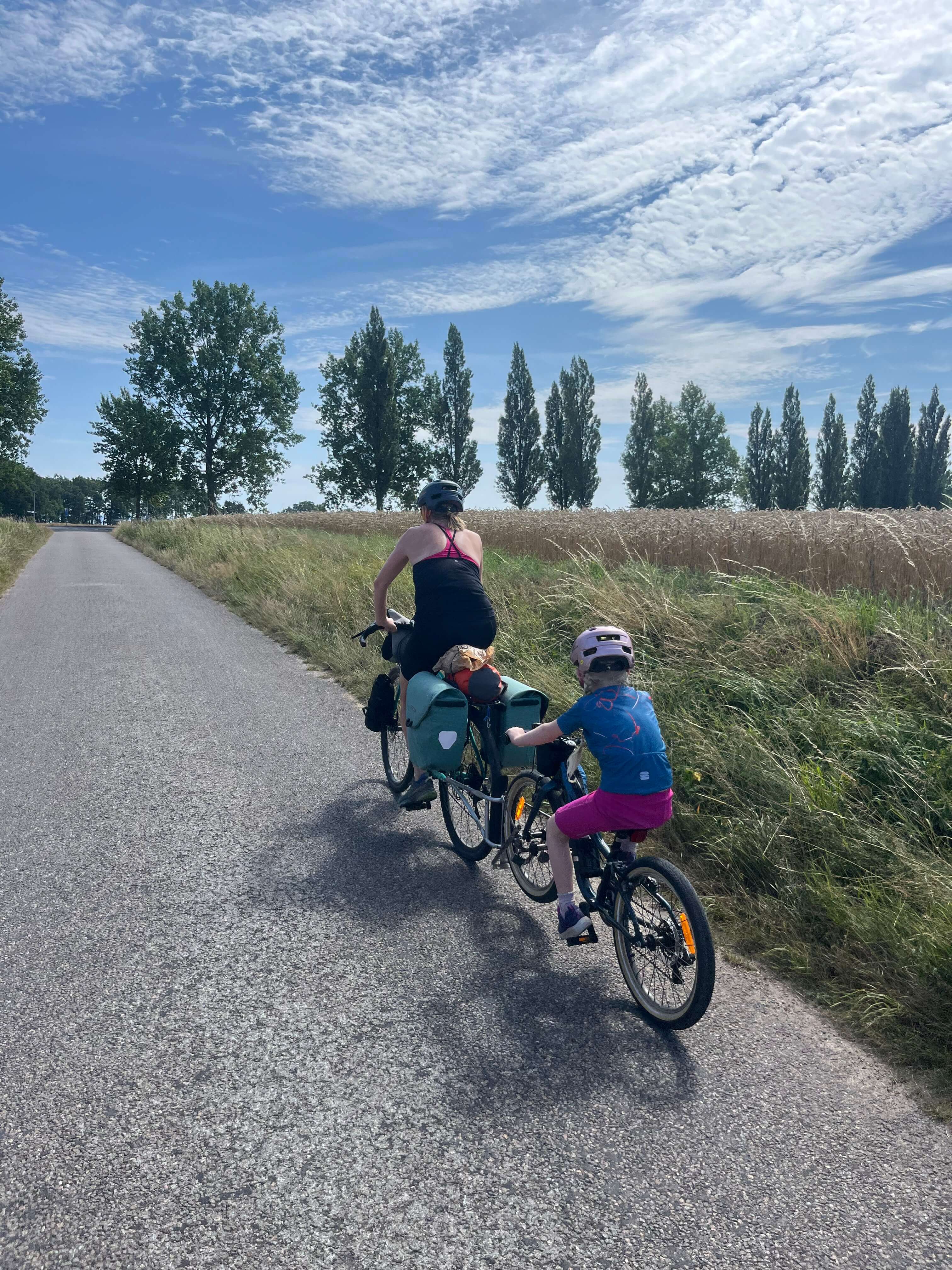 Ridgeback Dimension 20 kids bike being towed by a FollowMe Tandem along a pathway surrounded by grass and trees