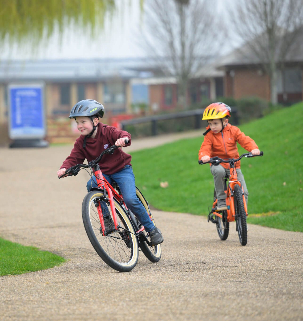 Two children riding ridgeback bikes around a corner on a paved pathway