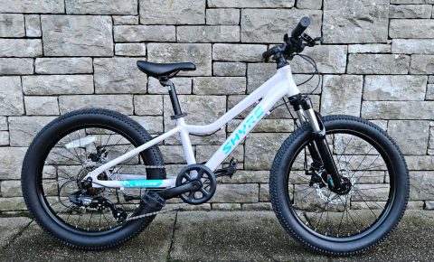 Shyre Eastie 20 kids bike in white leaning against a stone brick wall