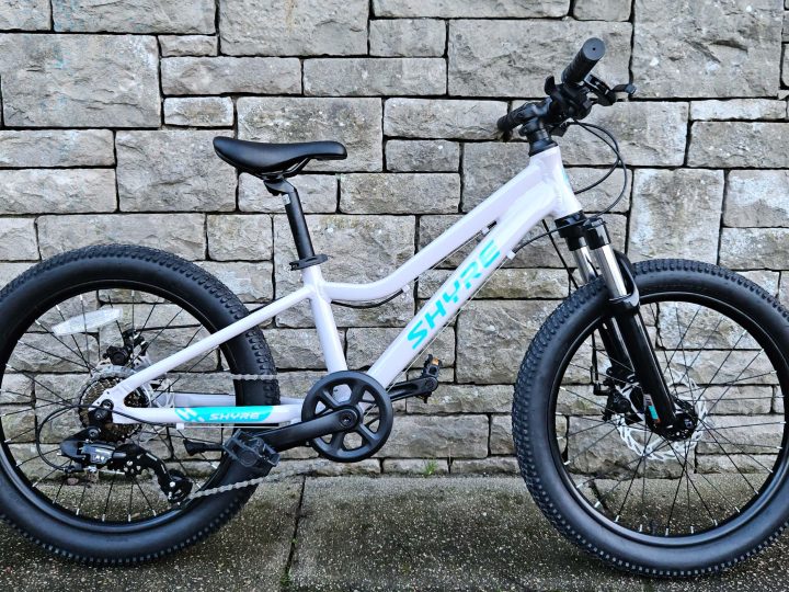 Shyre Eastie 20 kids bike in white leaning against a stone brick wall