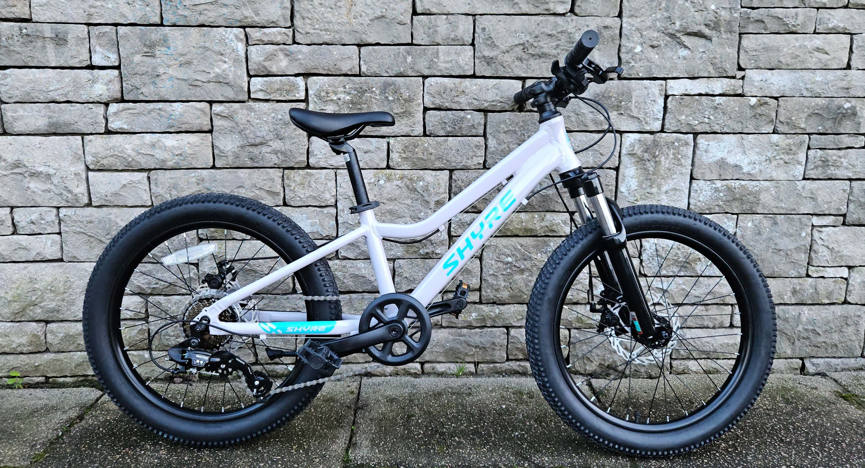 Shyre Eastie 20 kids bike in white leaning against a stone brick wall