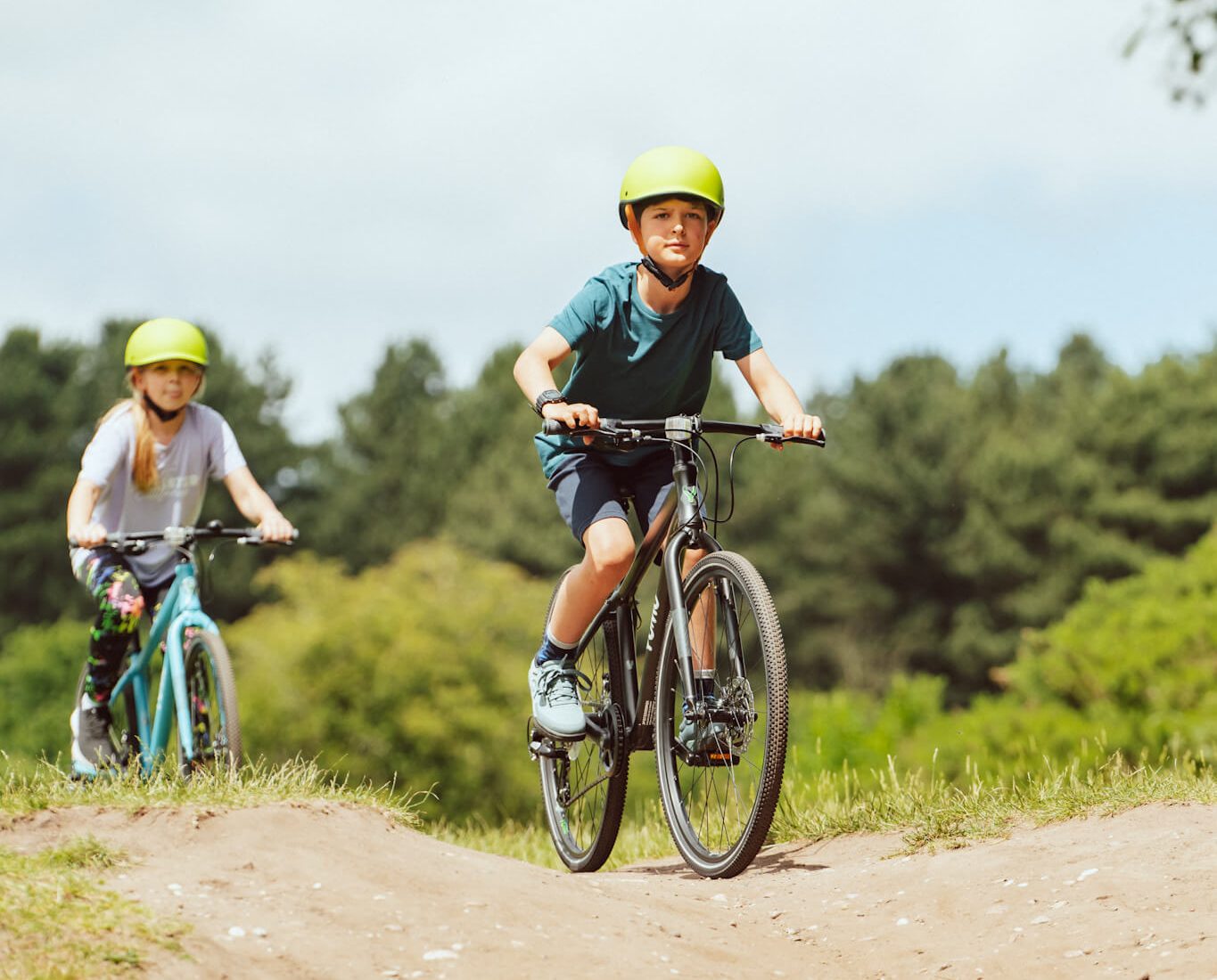 2 kids riding the Yomo kids bikes in black and blue along a dirt track