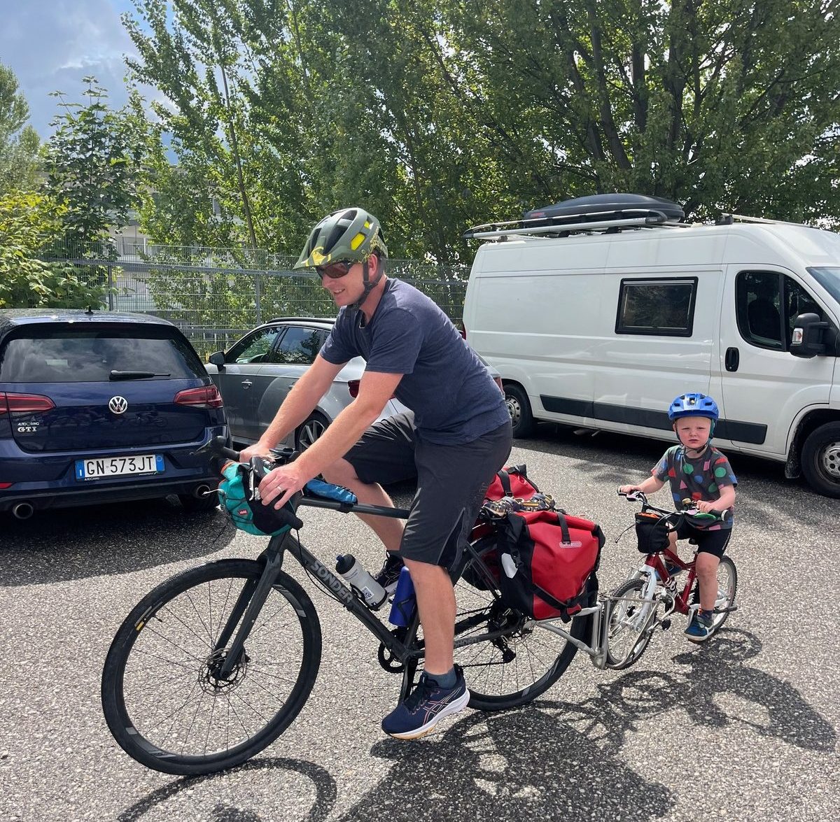 Adult and child cycling in a car park abroad away from their broken down campervan to start cycling back to the UK
