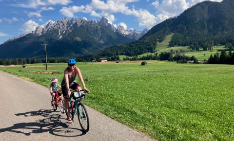 Adult and child cycling along a road in the Dolomites with the mountains in the background