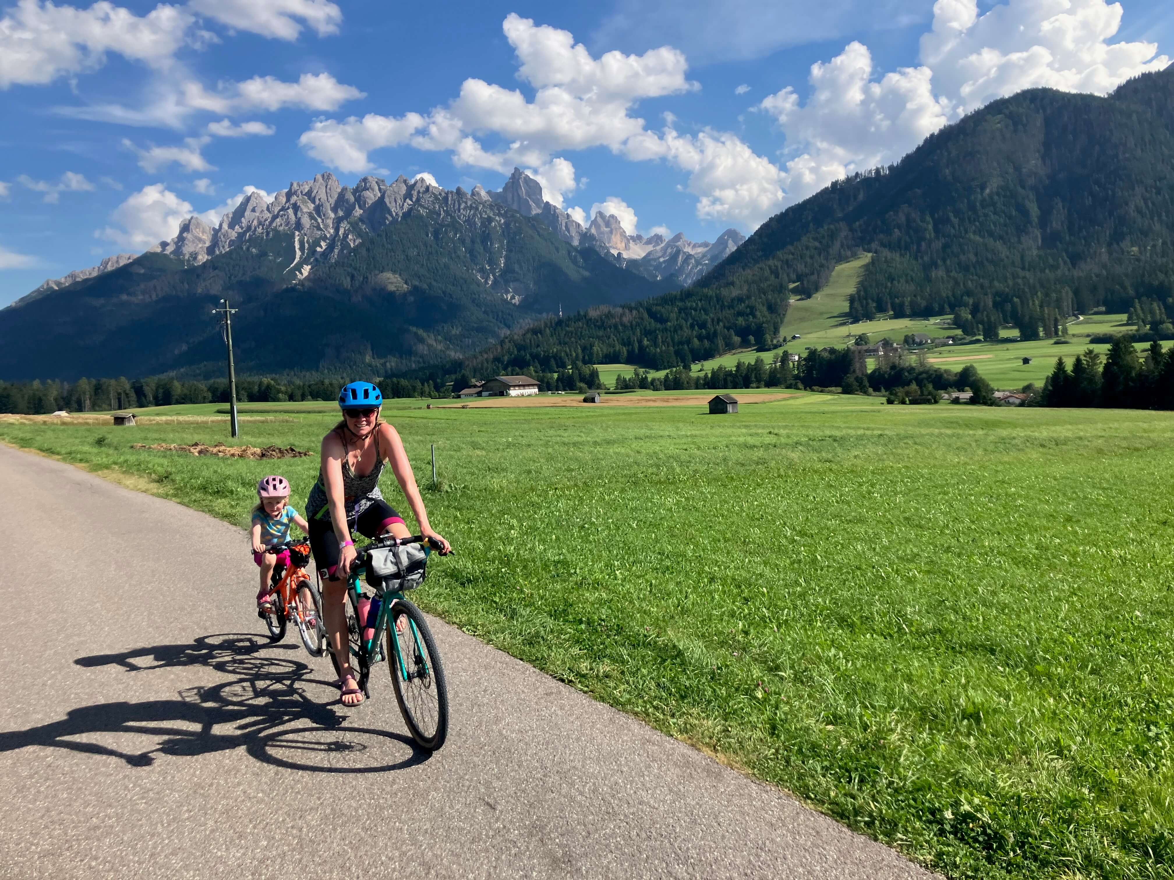 Adult and child cycling along a road in the Dolomites with the mountains in the background