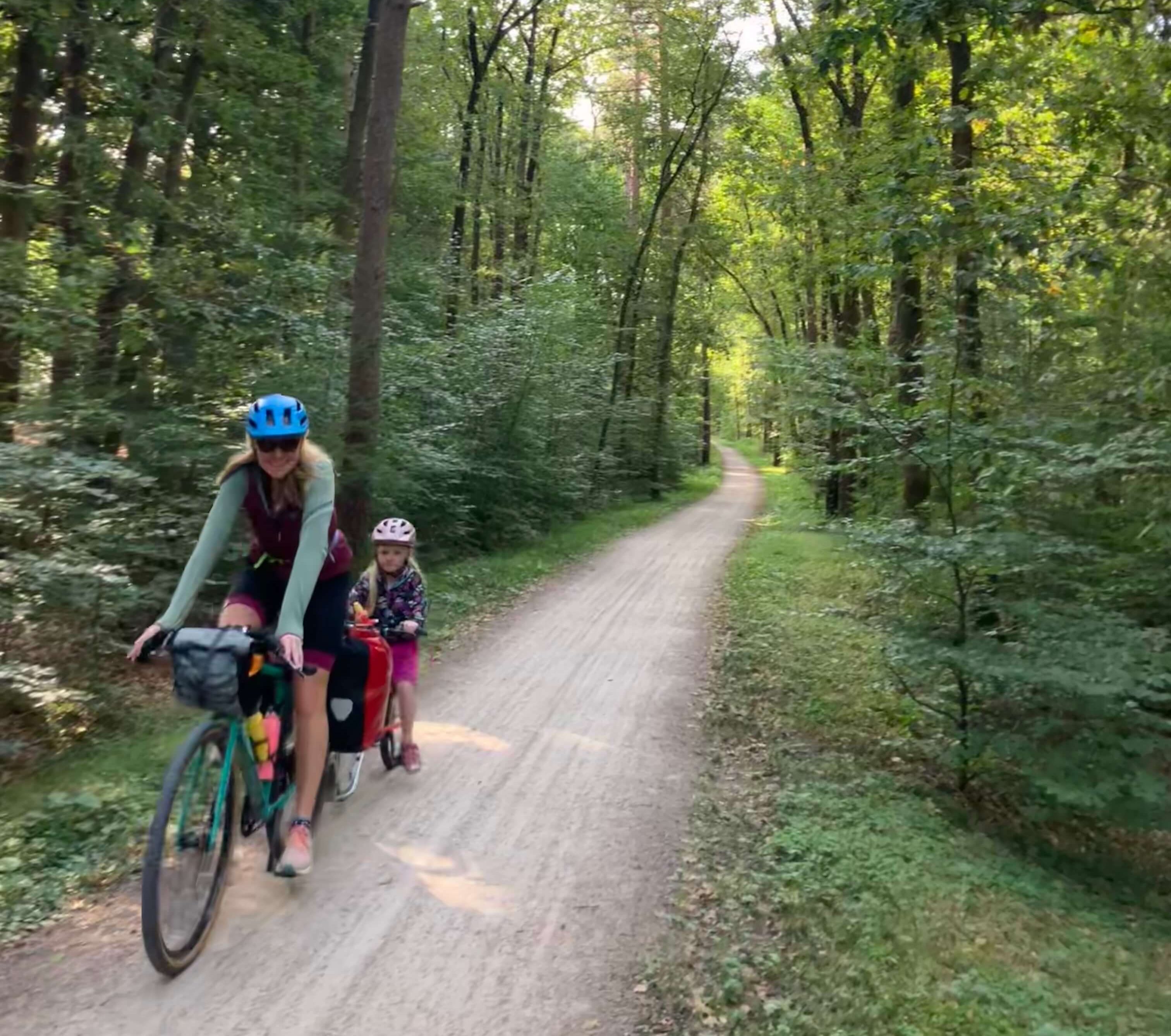 An adult and a child cycling through a woodland path