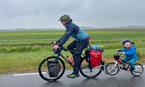 Adult towing a child on their own bike along a road in the countryside