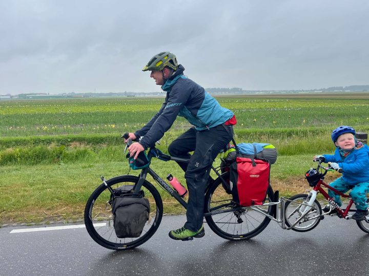 Adult towing a child on their own bike along a road in the countryside