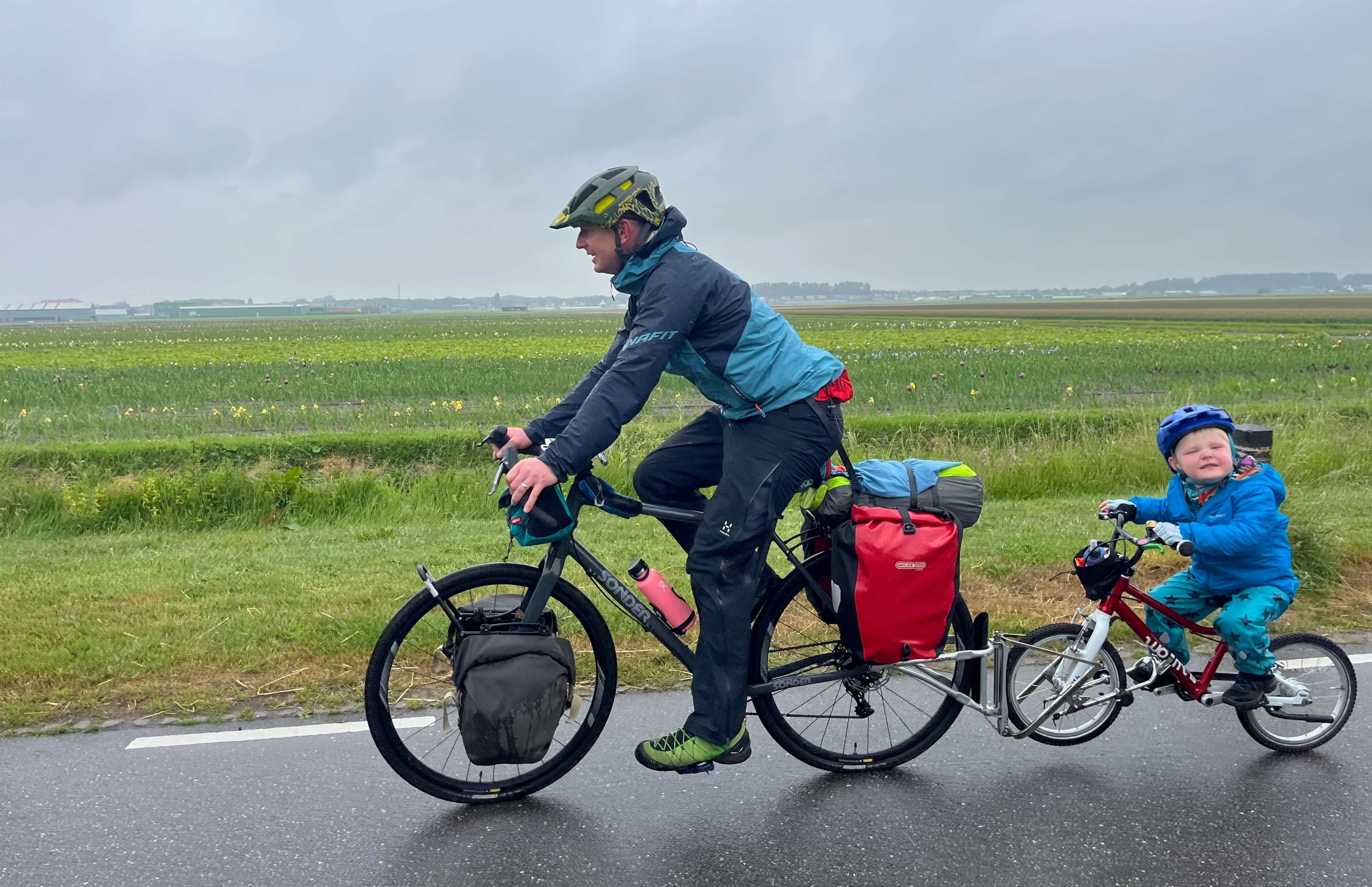 Adult towing a child on their own bike along a road in the countryside